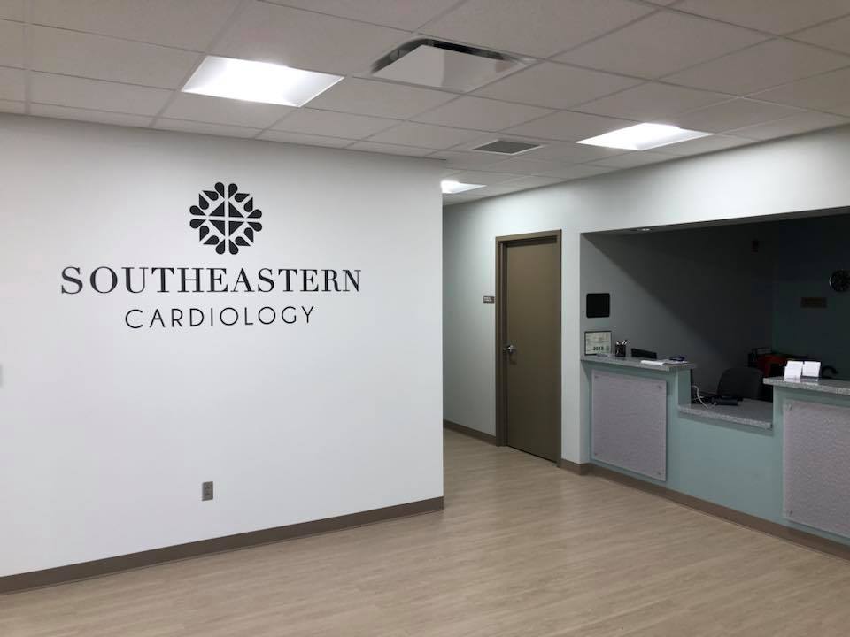 A clean, modern medical office lobby with Southeastern Cardiology written on the wall and a reception desk to the right. The space has light-colored floors and white walls.