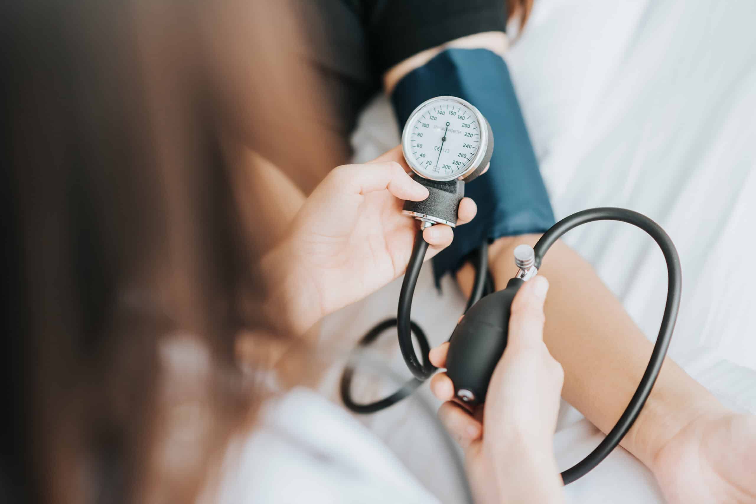 A healthcare professional measures a persons blood pressure using a manual sphygmomanometer and stethoscope with the cuff wrapped around the patients upper arm.